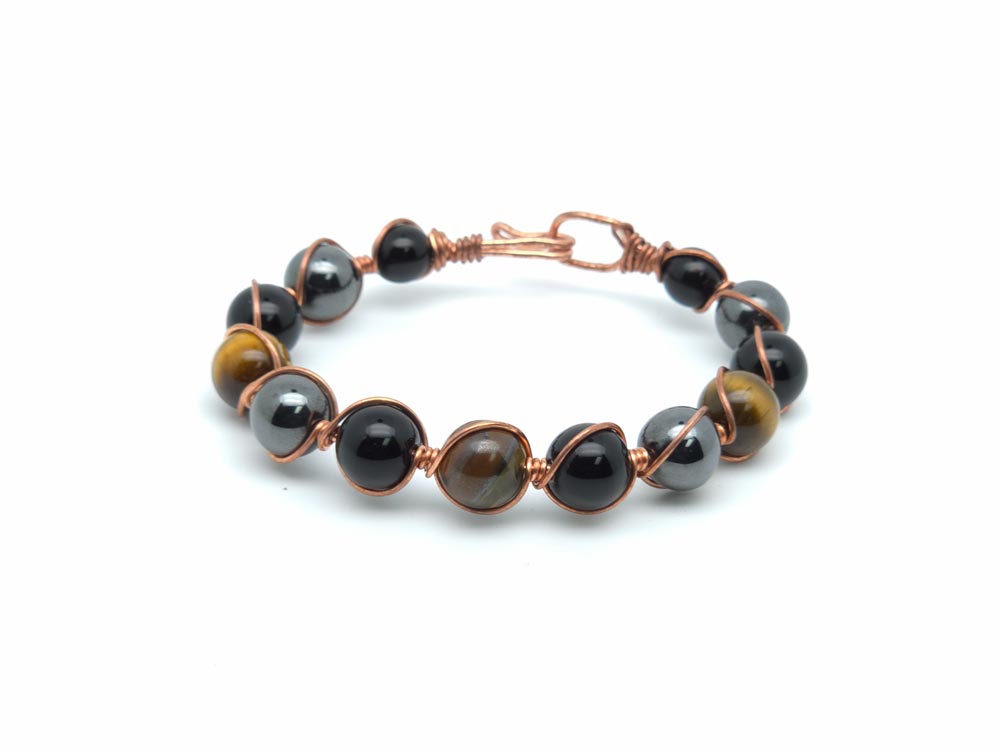 A beaded wire bracelet featuring polished round beads in black, dark gray, and brown tiger's eye, wrapped in copper-toned metal with a spring-ring clasp, shown on a white background.